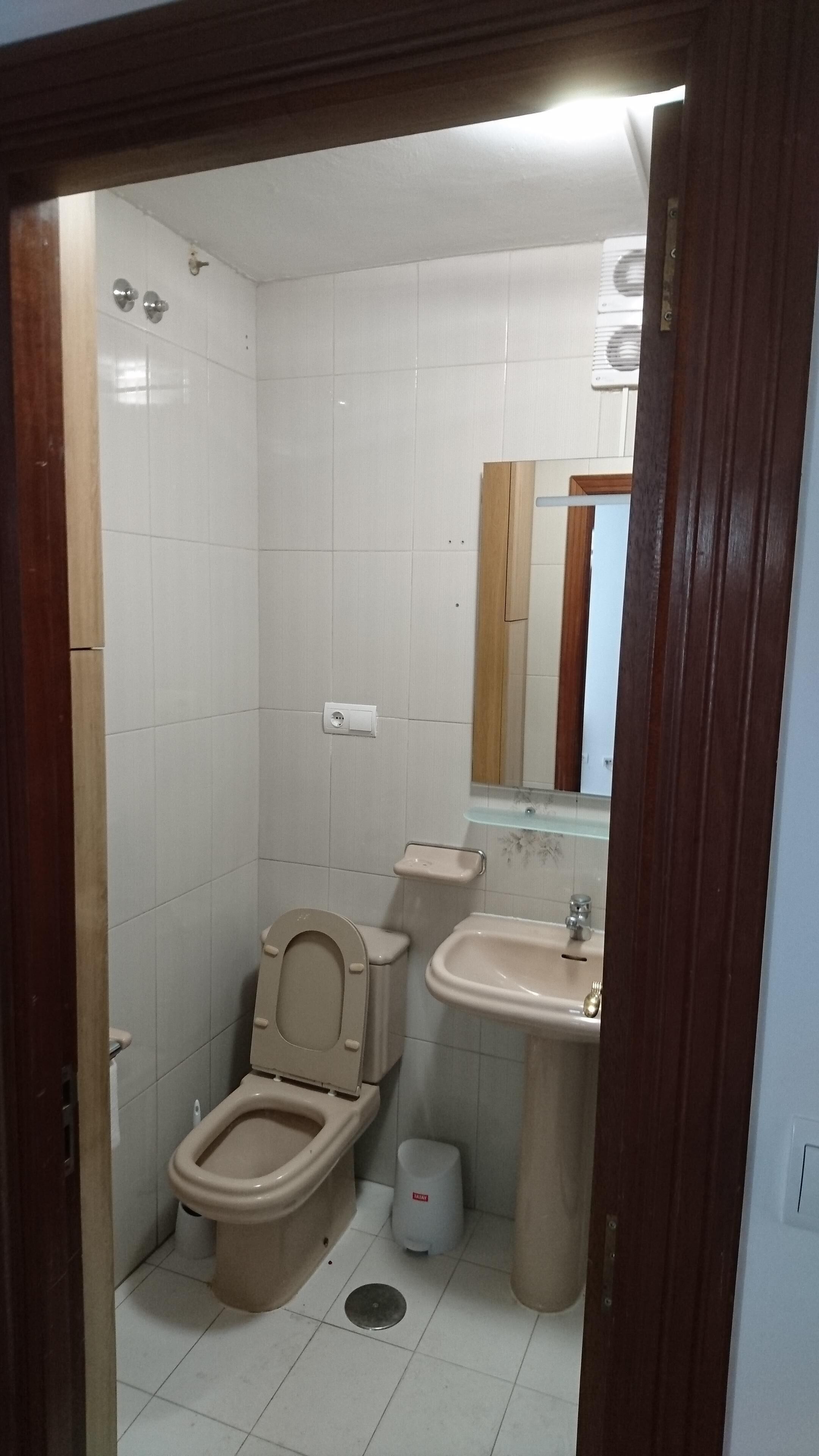 A small, compact bathroom with a toilet, sink, and mirror.