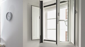 Une pièce avec un mur blanc, une horloge, un radiateur, un lit et une fenêtre avec des stores.