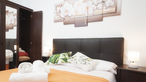 Une chambre d’hôtel comprenant un lit, une table de chevet, une armoire et un mur orné d’un tableau représentant des motifs floraux.