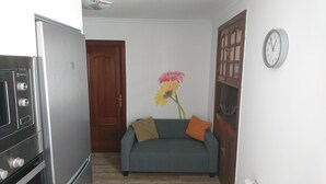 Un espace de vie compact comprenant un coin cuisine, un canapé, une porte en bois et une horloge murale.