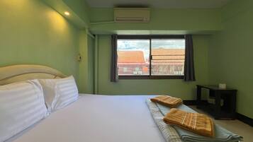 Une chambre d’hôtel avec un lit, des oreillers, une fenêtre avec des rideaux, une petite table et un appareil de climatisation.