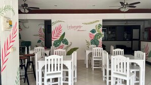 A dining area with white chairs and tables, a ceiling fan, and a wall with tropical leaf patterns. - Bella Bella House (Bangkok)