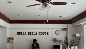A reception area with a ceiling fan, a clock, and a sign reading "Bella Bella House". - Bella Bella House (Bangkok)