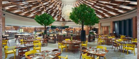 A spacious restaurant with yellow and brown chairs, a central chandelier, and a modern ceiling design.
