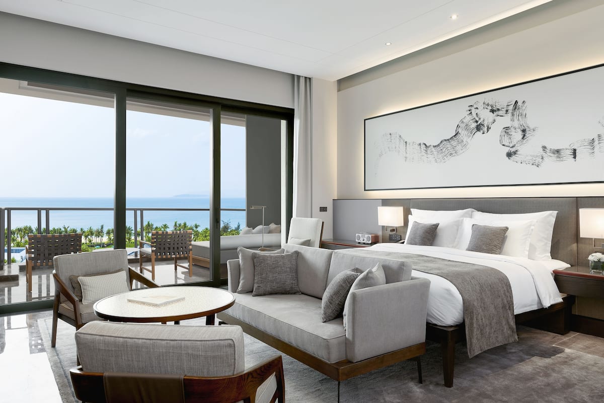 Une chambre d’hôtel moderne dotée d’un grand lit, d’un balcon avec vue et d’un grand tableau abstrait accroché au mur.