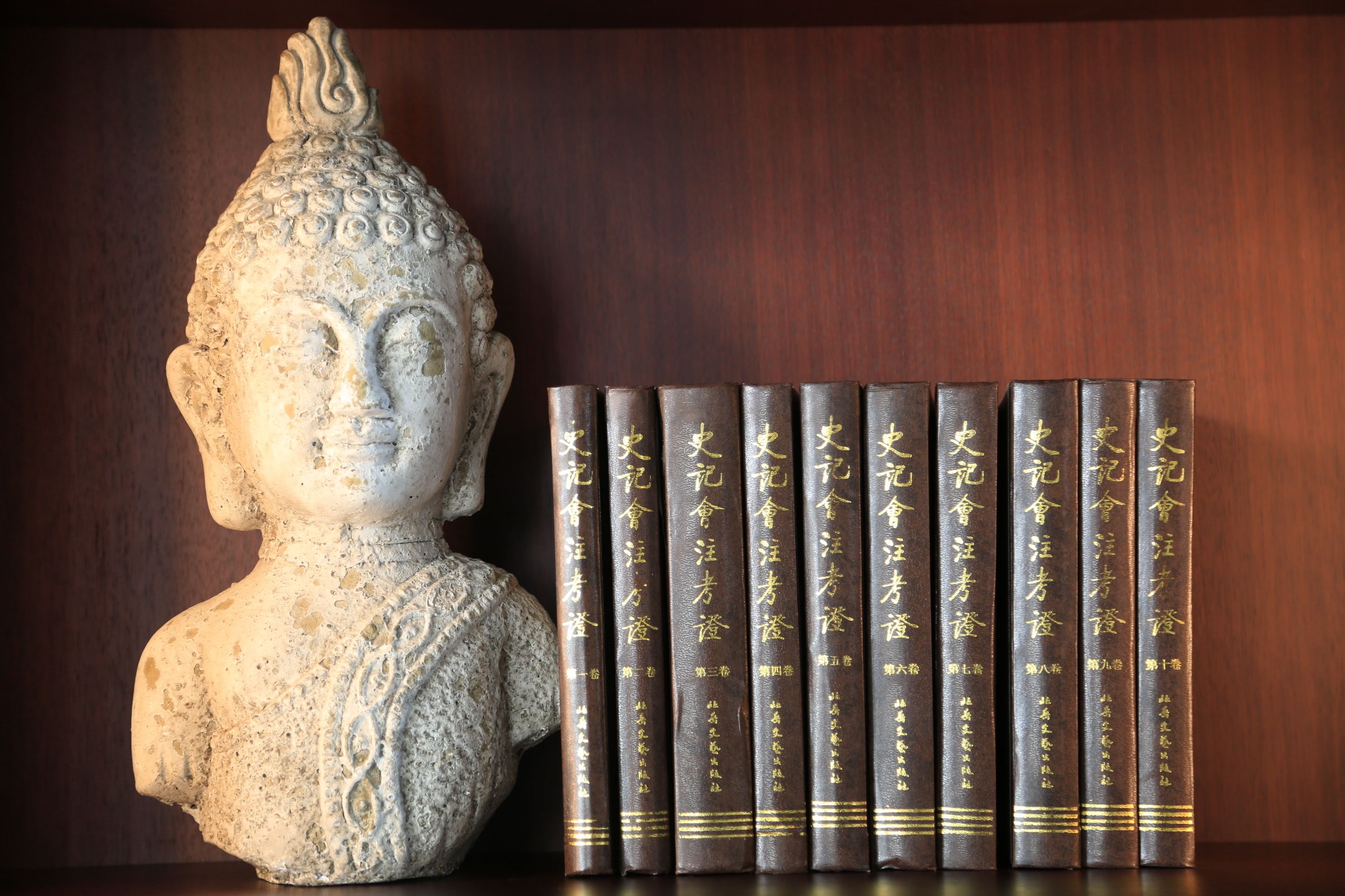 Eine Büste und eine Reihe Bücher mit goldener Schrift auf einer Holzoberfläche.