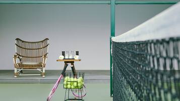Una cancha de tenis con una silla de mimbre, una mesa con botellas y una raqueta de tenis.