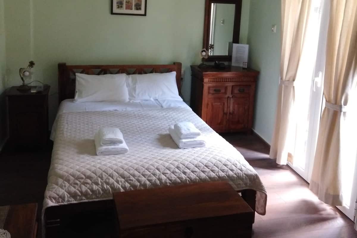 A neatly made bed with white linens, a wooden headboard, and a bedside table with a lamp. There is a wooden chest of drawers and a mirror on the wall.