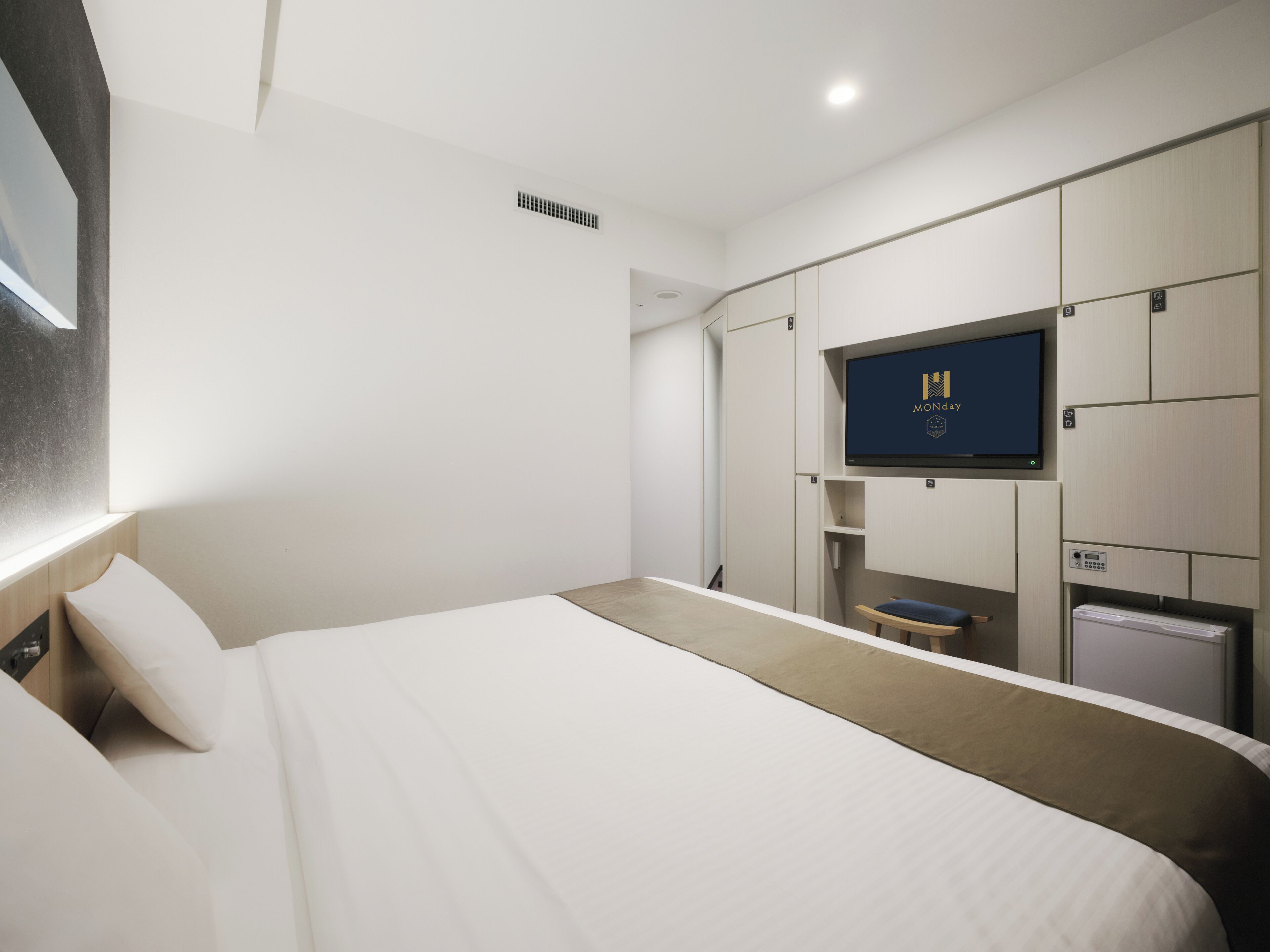 A modern hotel room with a large bed, a TV mounted on the wall, and a minibar.