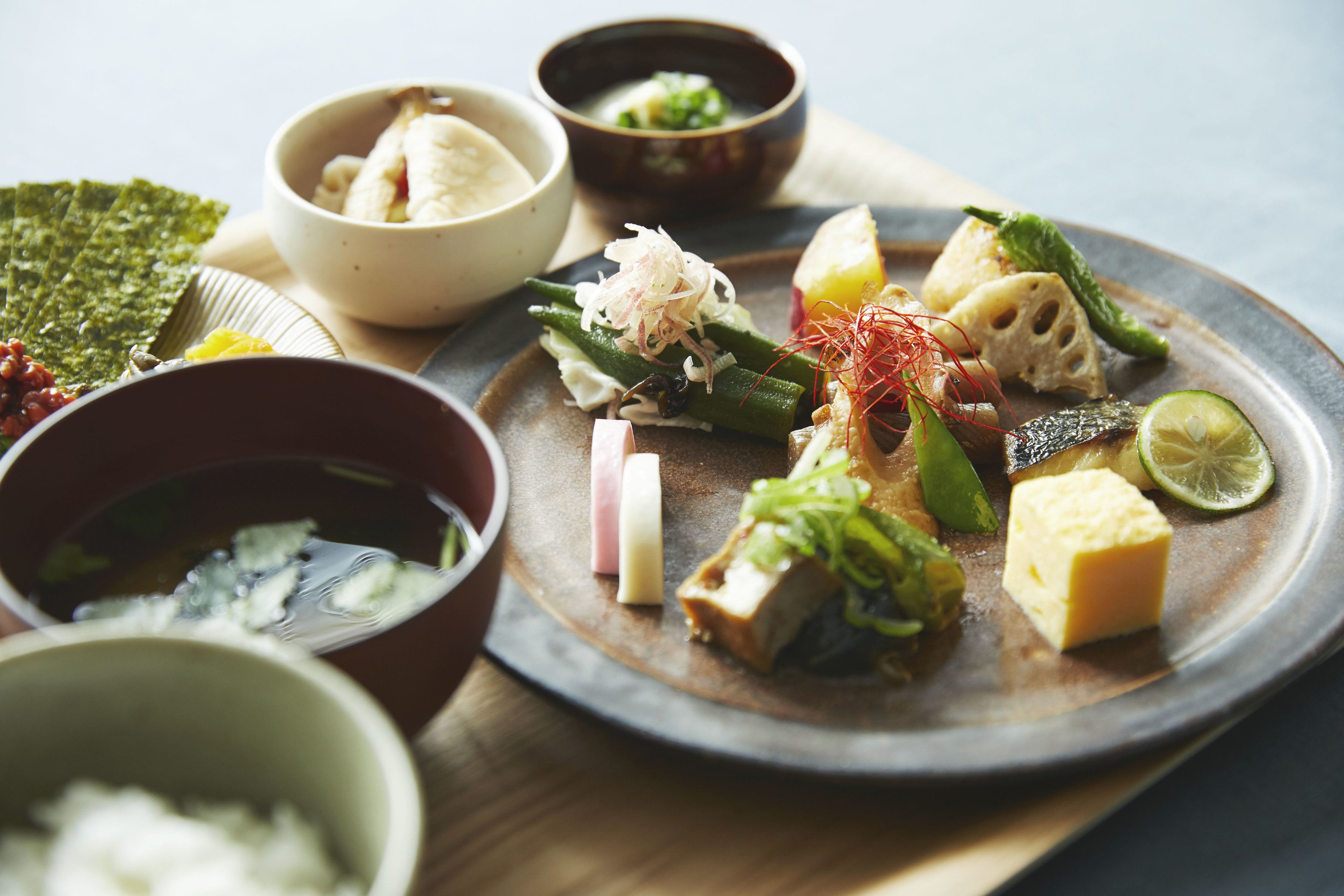 Una variedad de platillos en un plato, incluyendo tofu, verduras y posiblemente pescado, acompañados de pequeñas cazuelas de sopa y salsas.