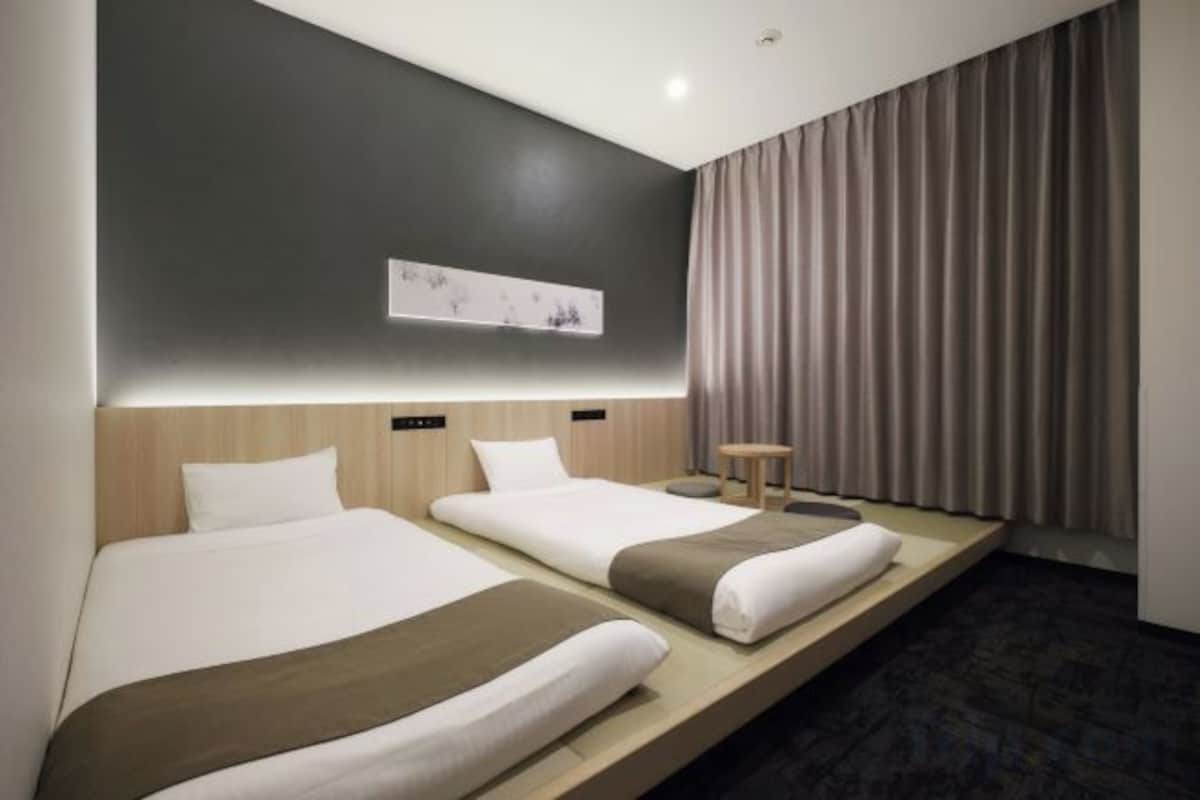 Une chambre d’hôtel avec deux lits, une petite table et une œuvre d’art accrochée au mur.