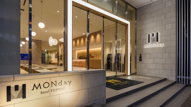 Das moderne Äußere des Monday Hotels, darunter ein Glastürbereich, ein sichtbarer Küchenbereich und ein Schild mit dem Hotelnamen.