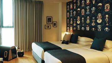 A hotel room with two beds, a large window with curtains, and a wall with a pattern of dog masks.