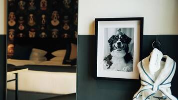 Una habitación de hotel con una cama, un cuadro con una imagen de un perro y una bata colgada en la pared.