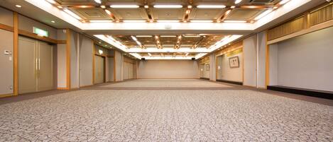 Un salón de conferencias amplio y vacío, con alfombra estampada, paneles de madera e iluminación empotrada, además de detalles decorativos.