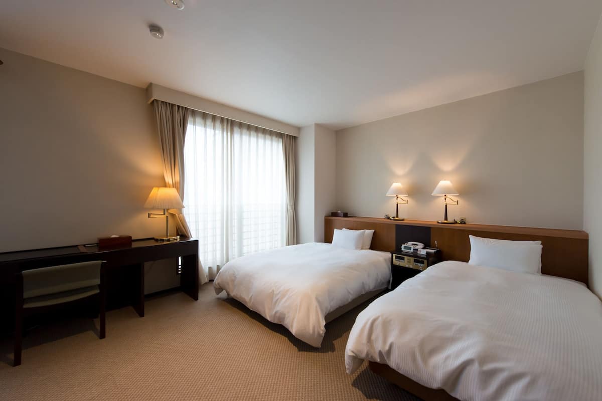 Una habitación de hotel con dos camas, un escritorio y lámparas.