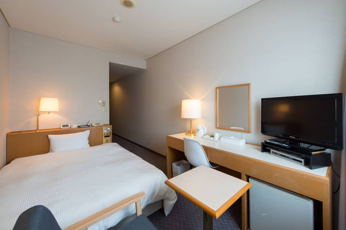 Una habitación de hotel con cama, escritorio, silla, televisor y un refrigerador pequeño.