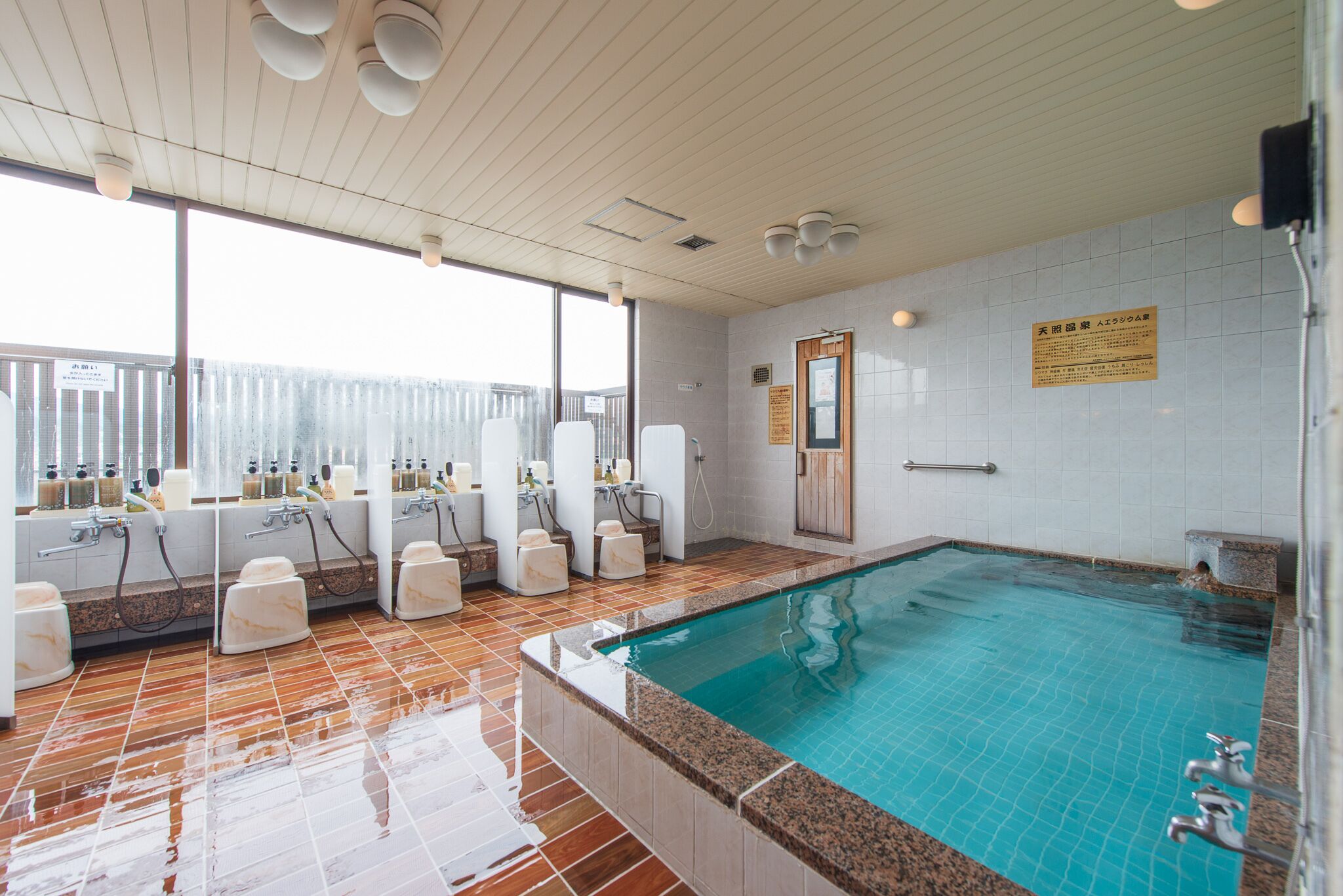 A swimming pool area with multiple changing rooms, a large window, and a tiled floor.