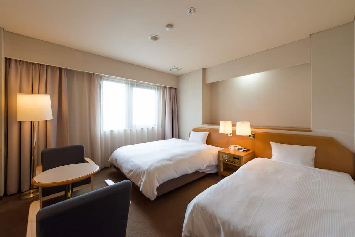 Habitación de hotel con dos camas, un escritorio y una silla. Hay dos mesitas de noche con lámparas.