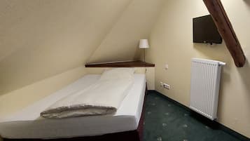 A small, single-bed room with a wooden headboard, a bedside table with a lamp, and a radiator on the wall.