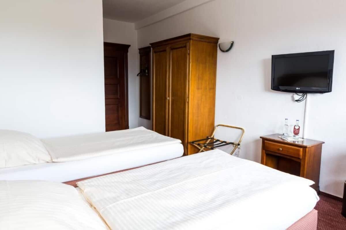 Een hotelkamer met twee bedden, een houten kledingkast, een televisie en een klein tafeltje met een fles.