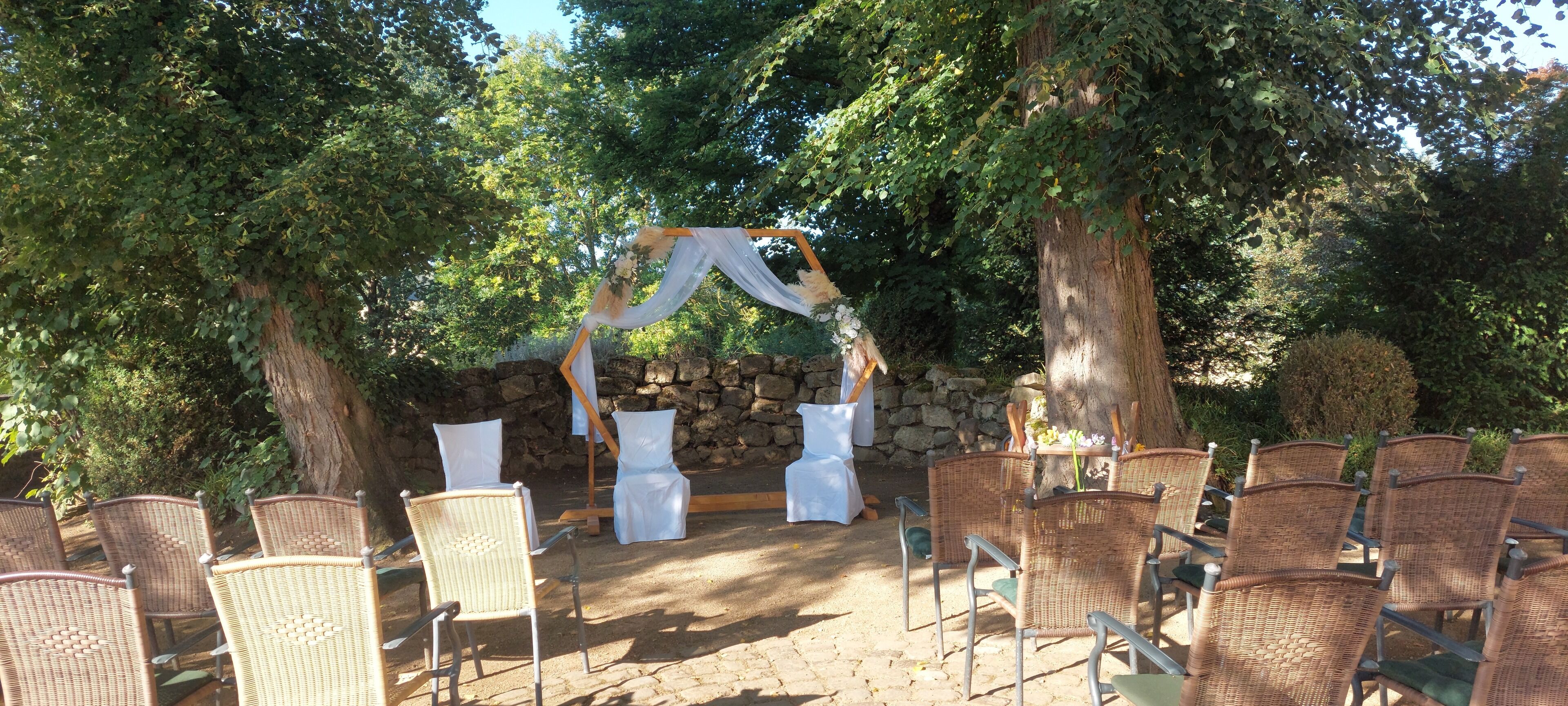 Montaje para boda al aire libre con sillas de mimbre y un fondo de pared de piedra.