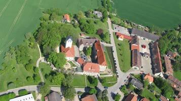 An aerial view of a village with traditional buildings, green fields, and a central square.