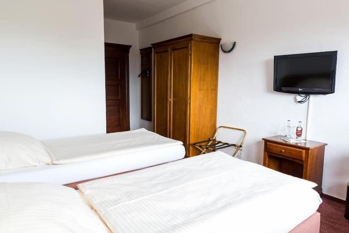 A hotel room with two beds, a wardrobe, a television, and a small table with a bottle.
