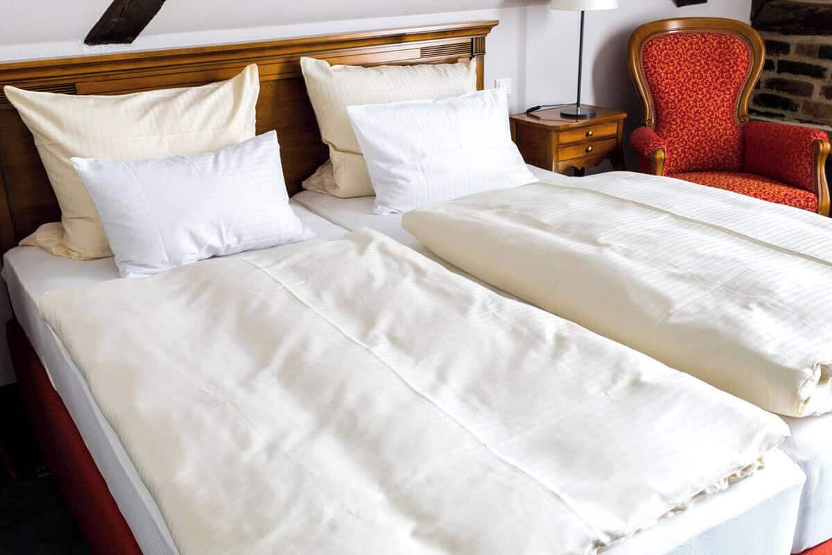 Een tweepersoonsbed met witte lakens, een houten hoofdbord en een rode stoel met een gestreept kussen.