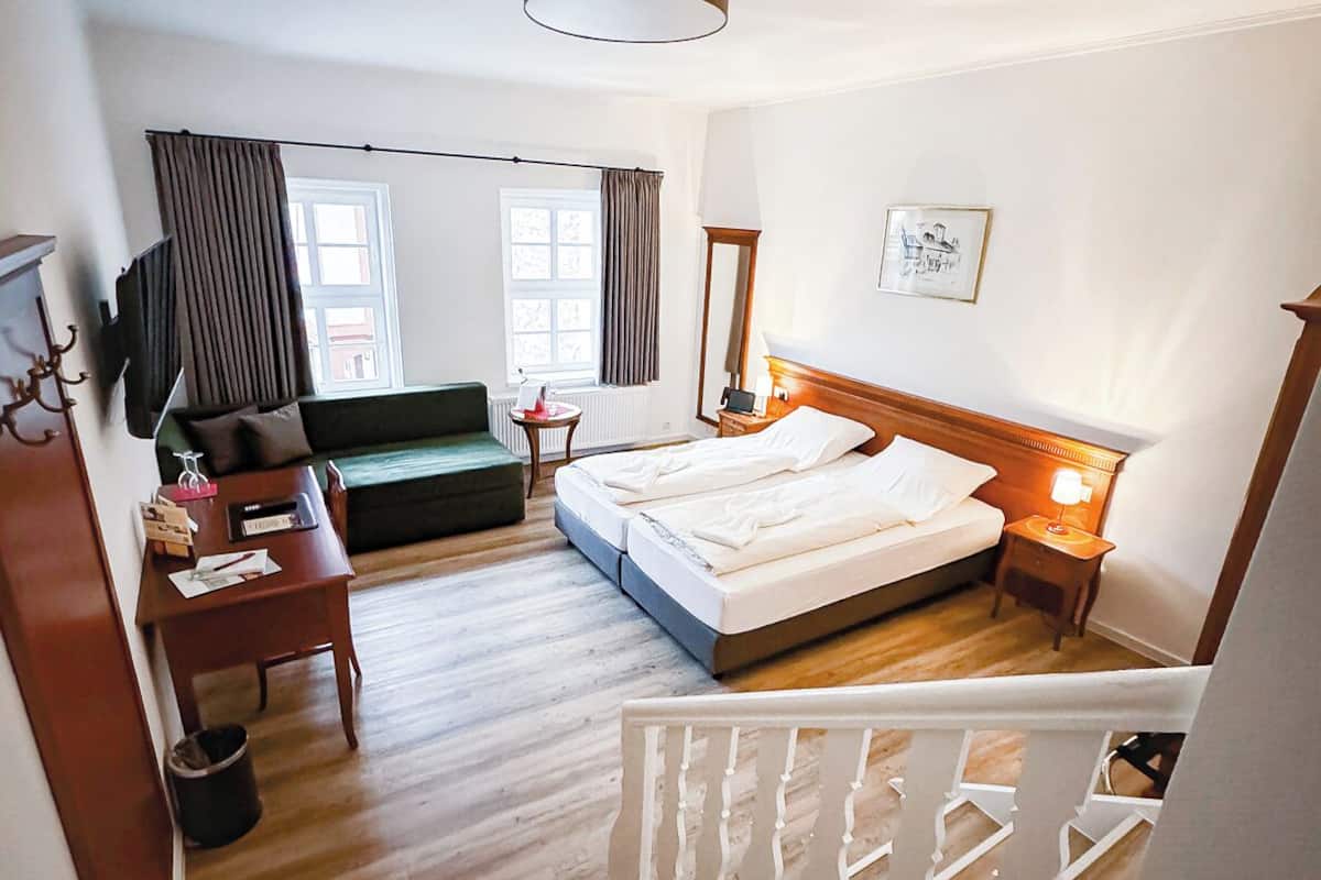 Een slaapkamer met een bed, een bureau, een stoel, een bank, een televisie en een raam.