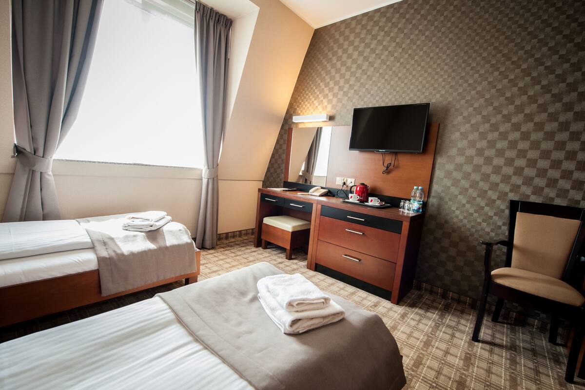 Een hotelkamer met twee bedden, een bureau met stoel, een televisie en een geruit muur.