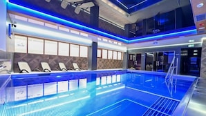 A modern indoor swimming pool with blue lighting, lounge chairs, and a mezzanine level. - Hotel Rudnik (Grudziadz)