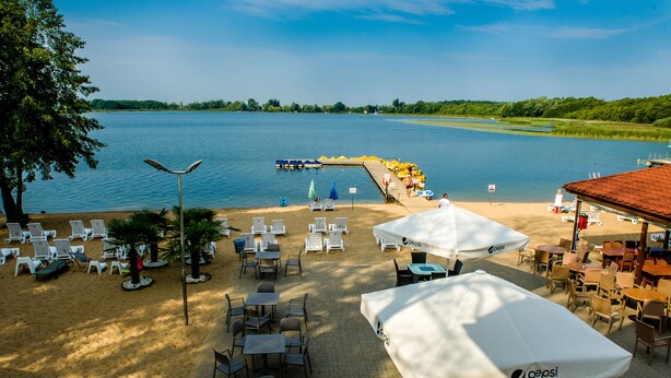 A lakeside outdoor seating area with tables and chairs, umbrellas, and a view of the lake. - Hotel Rudnik (Grudziadz)