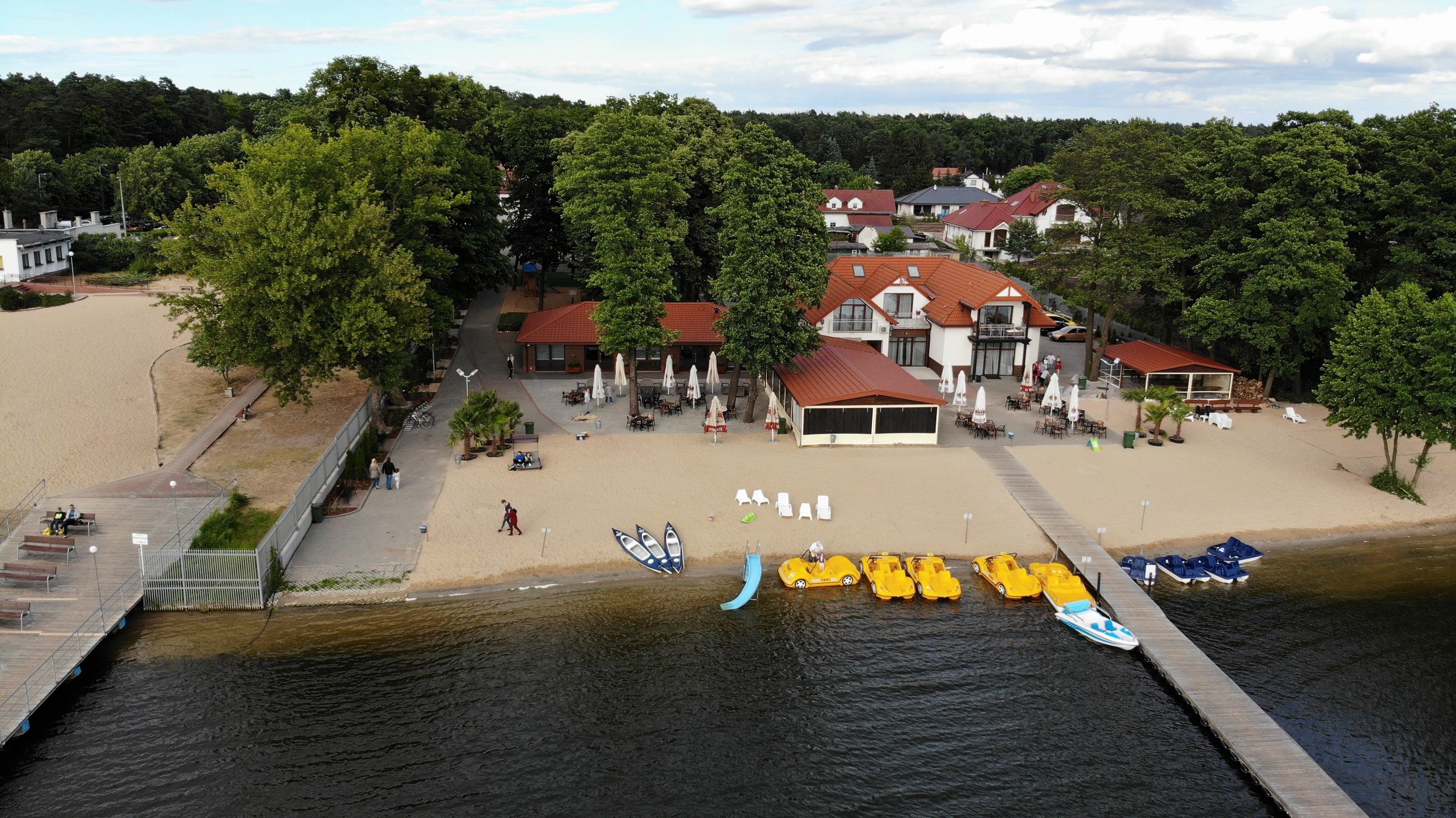A lakeside hotel with a sandy beach, boats, and a dock.
