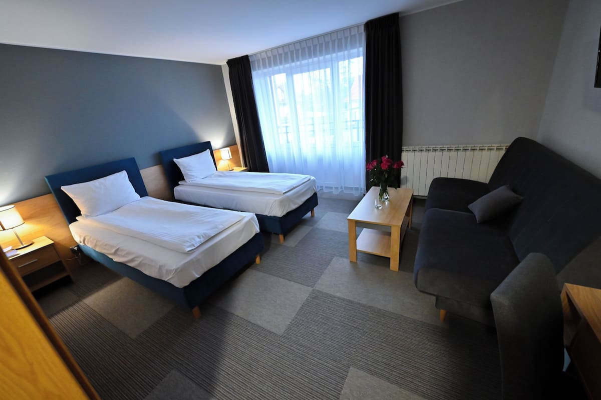 Een hotelkamer met twee eenpersoonsbedden, een slaapbank, een tafeltje en een raam met gordijnen.