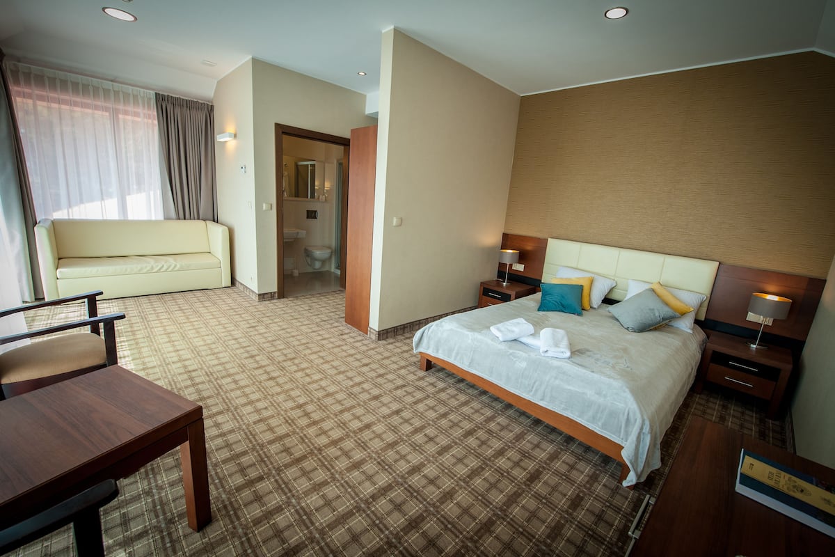 Een hotelkamer met een bed, nachtkastjes, een bureau, een stoel en een badkamer zichtbaar door een geopende deur.