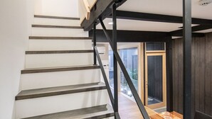 Een trap met houten treden en zwarte metalen leuningen, leidend naar een kamer met een houten bank en een raam.