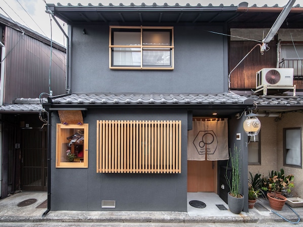A traditional Japanese house with a tiled roof, a wooden window, and a small entrance with a sliding door.