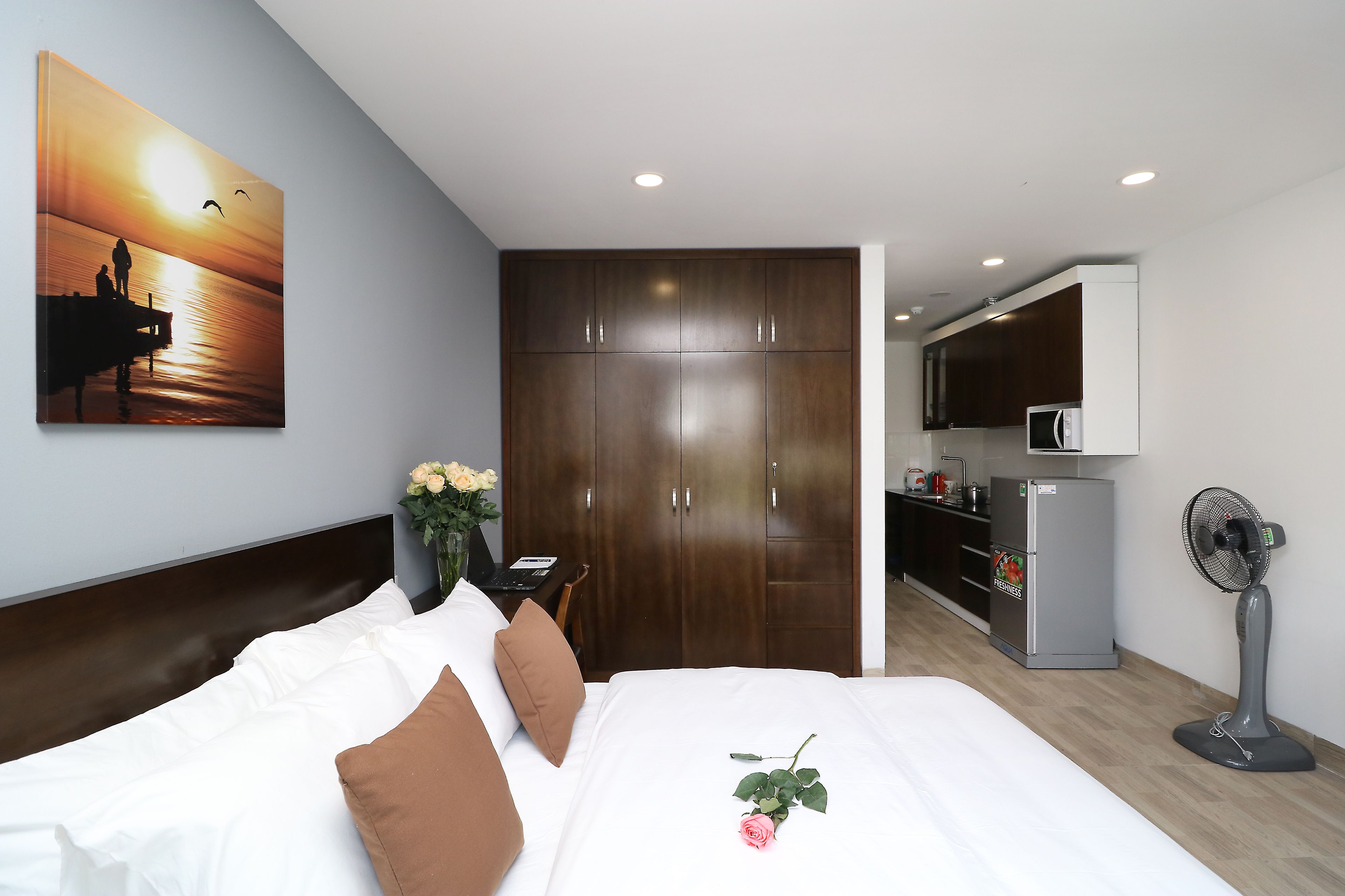 A hotel room with a bed, a desk, a wardrobe, a kitchenette, and a large window.