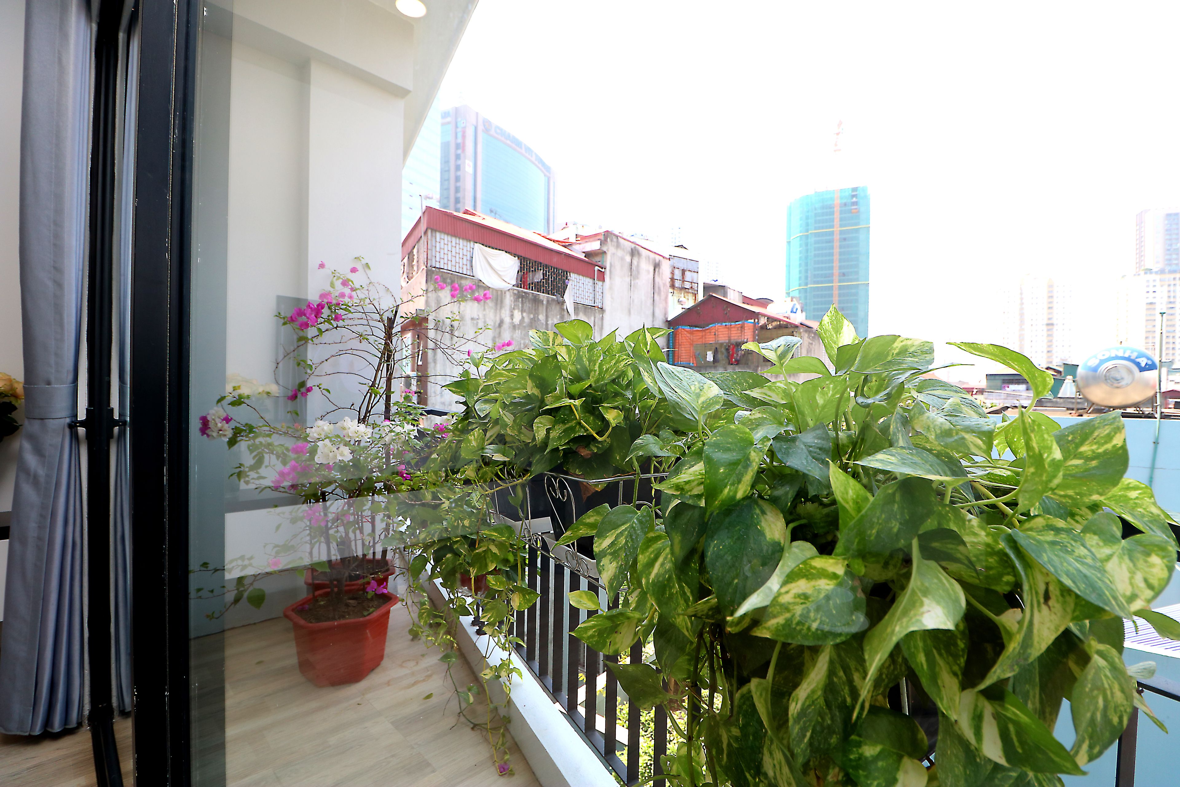 Varanda com plantas em vasos, vista para edifícios da cidade e grade de metal.