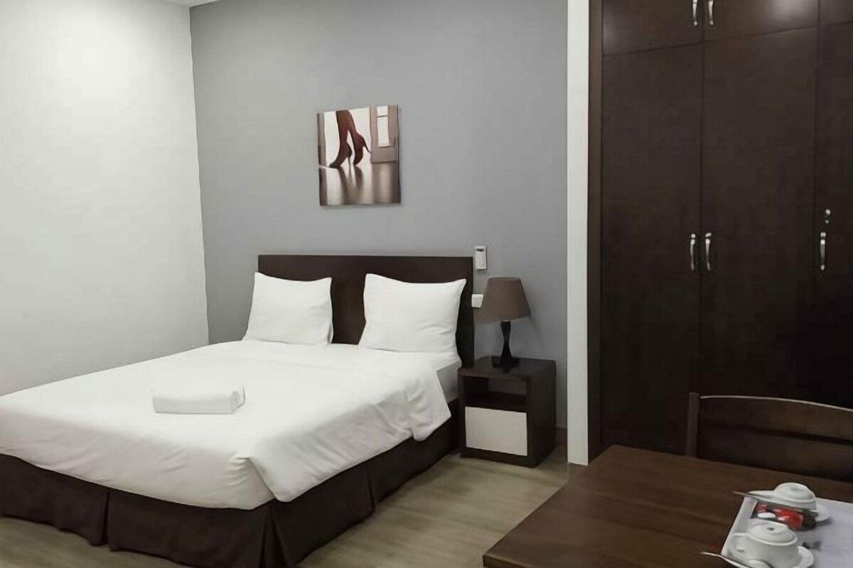 Una camera d'albergo con un letto, un comodino con una lampada, un armadio e un tavolo da pranzo con tazze e piattini.