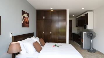 Habitación de hotel con cama, mesita de noche, lámpara, ventilador, microondas y kitchenette.