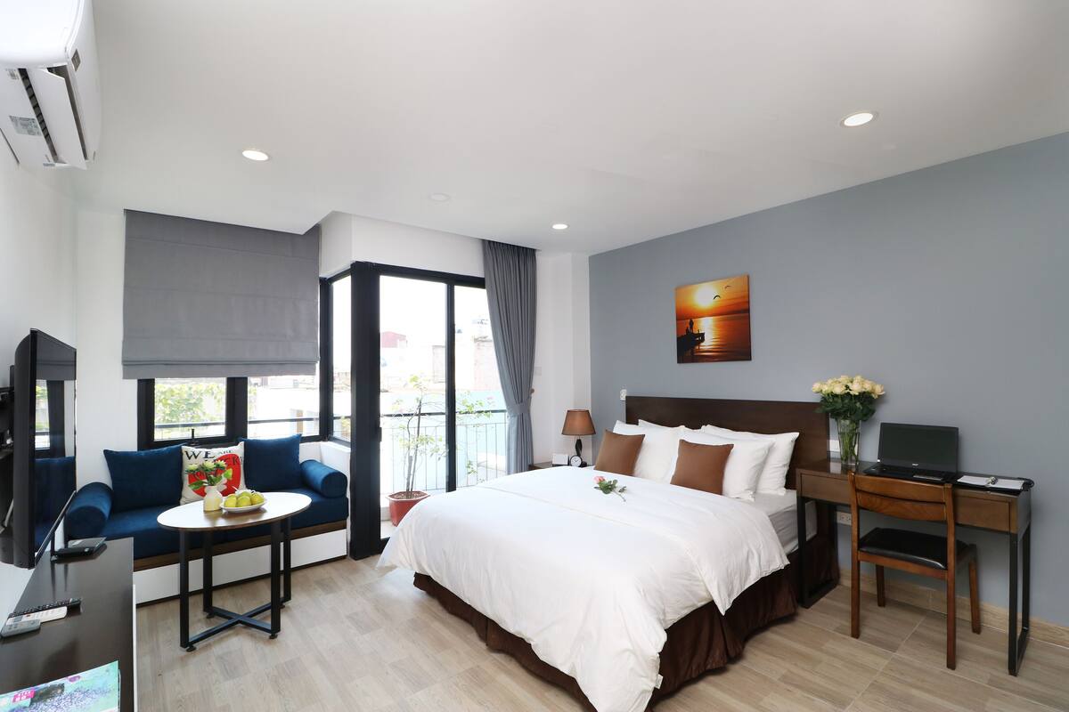 Ett modernt hotellrum med en stor säng, en soffa, ett skrivbord med en bärbar dator, en tv och en balkong med utsikt.