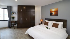 Een hotelkamer met een groot bed, een bureau met stoel, een kledingkast, een nachtkastje met lamp, en een schilderij van een zonsondergang aan de muur.
