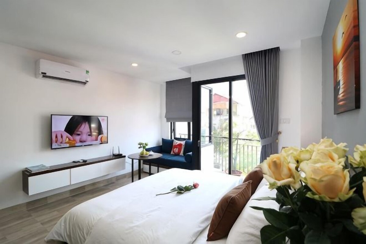 A modern hotel room with a large bed, a flat-screen TV, a sofa, and a balcony with a view.