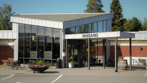 A modern building with a sign reading "INNGANG" and a covered entrance area with outdoor seating. - Slobrua Gjestegård (Sor-Odal)