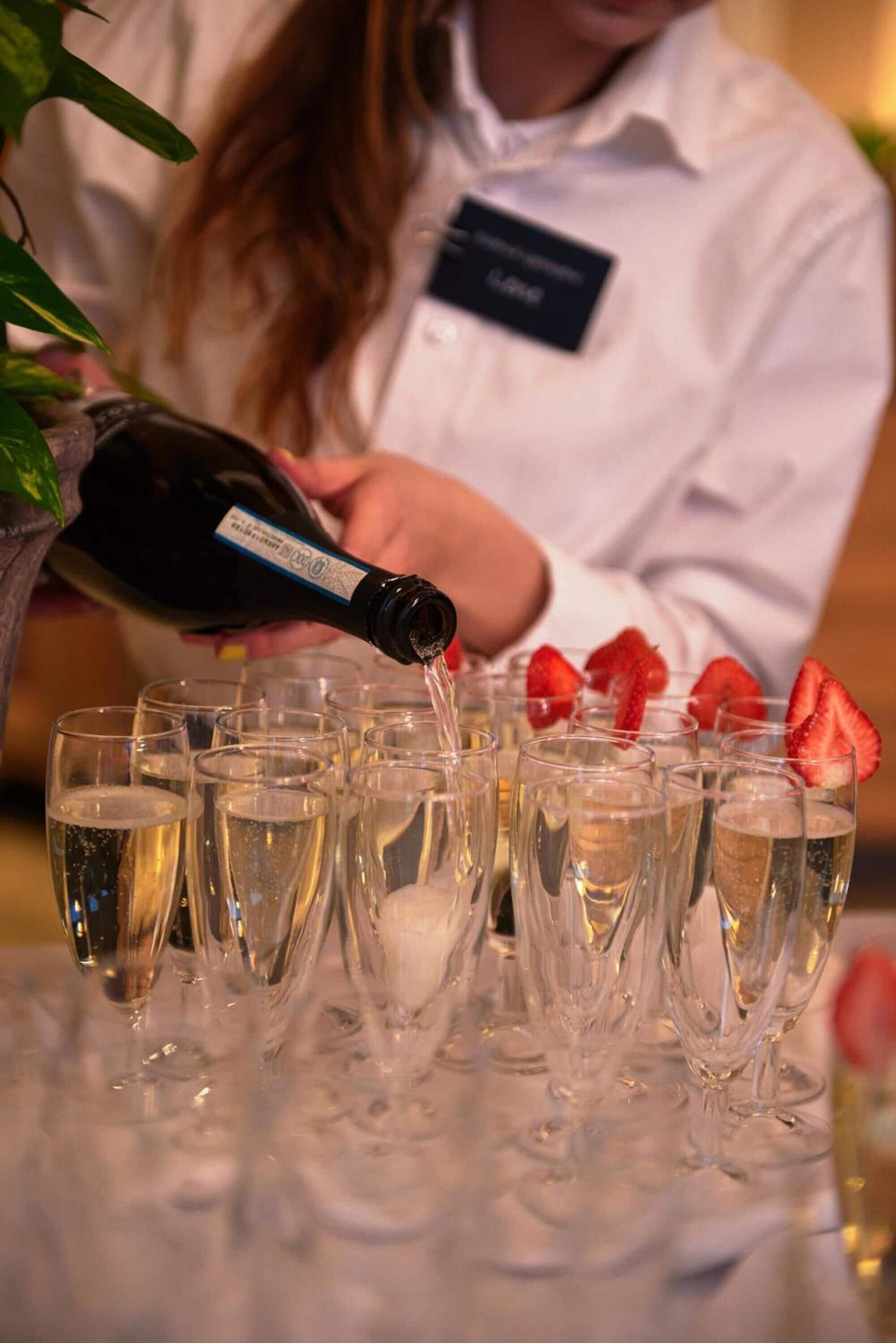 En person hælder champagne i glas med jordbær.
