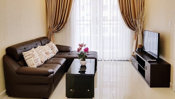A modern living room with a leather sofa, a glass coffee table, and a flat-screen TV on a wooden stand. - Florita SGN Green Living (Ho Chi Minh City)