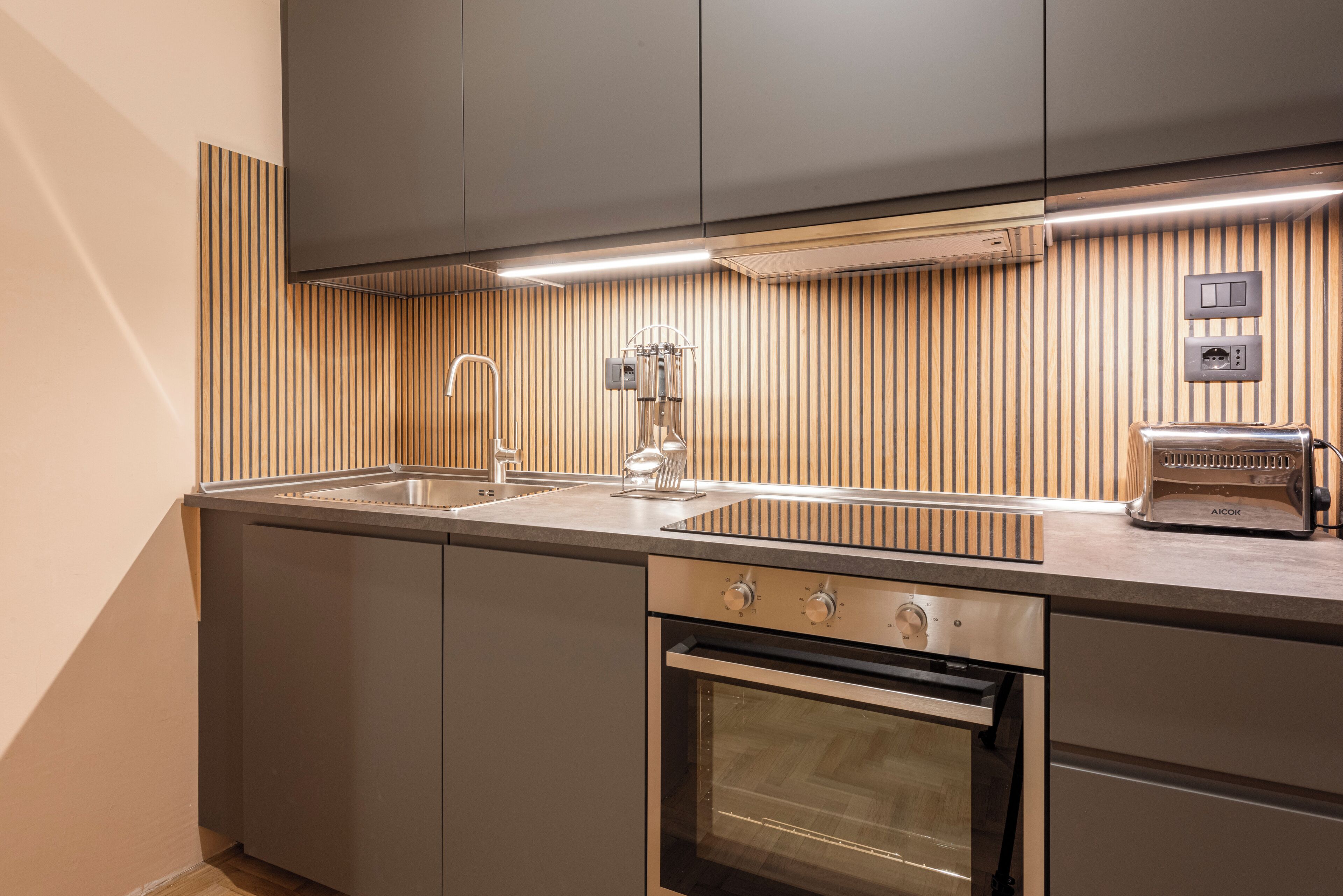 A modern kitchen with a built-in oven, stainless steel appliances, and a wooden backsplash.