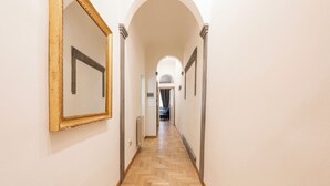 A hallway with a herringbone floor, white walls, and a large mirror on the left. - Santa Croce Retreat by MMega (Florence)